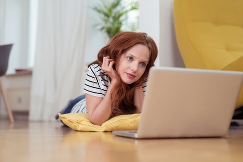 Pretty Young Woman Watching Movie on Laptop Computer Seriously While Lying on the Floor at the Home Living Room.-1